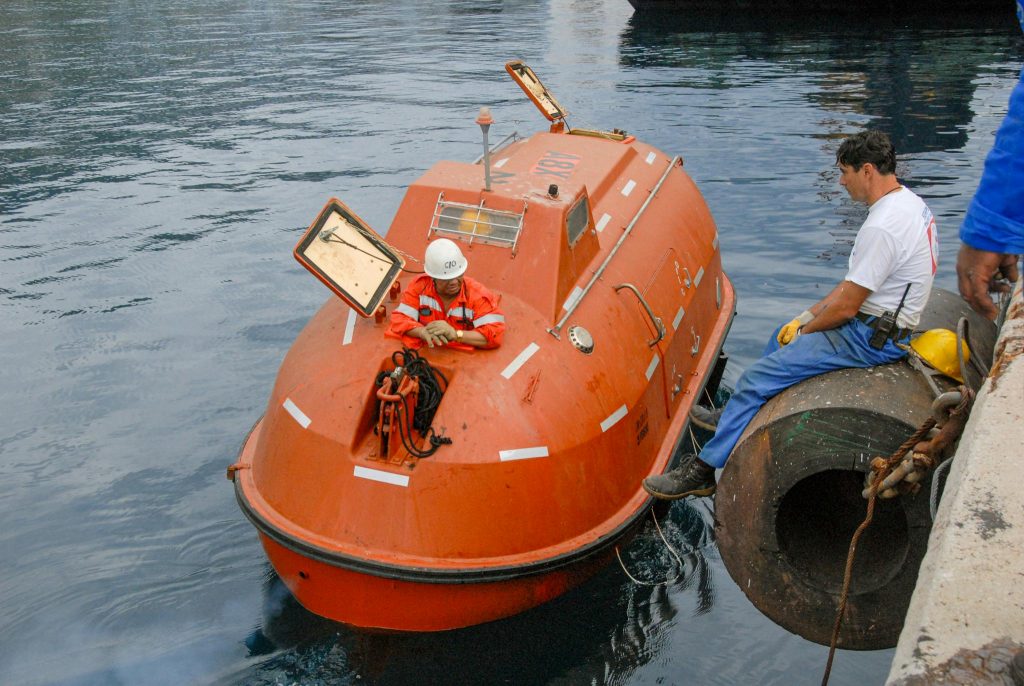 Crew members prepare a lifeboat for launch at a harbor. Maritime safety equipment and procedures.