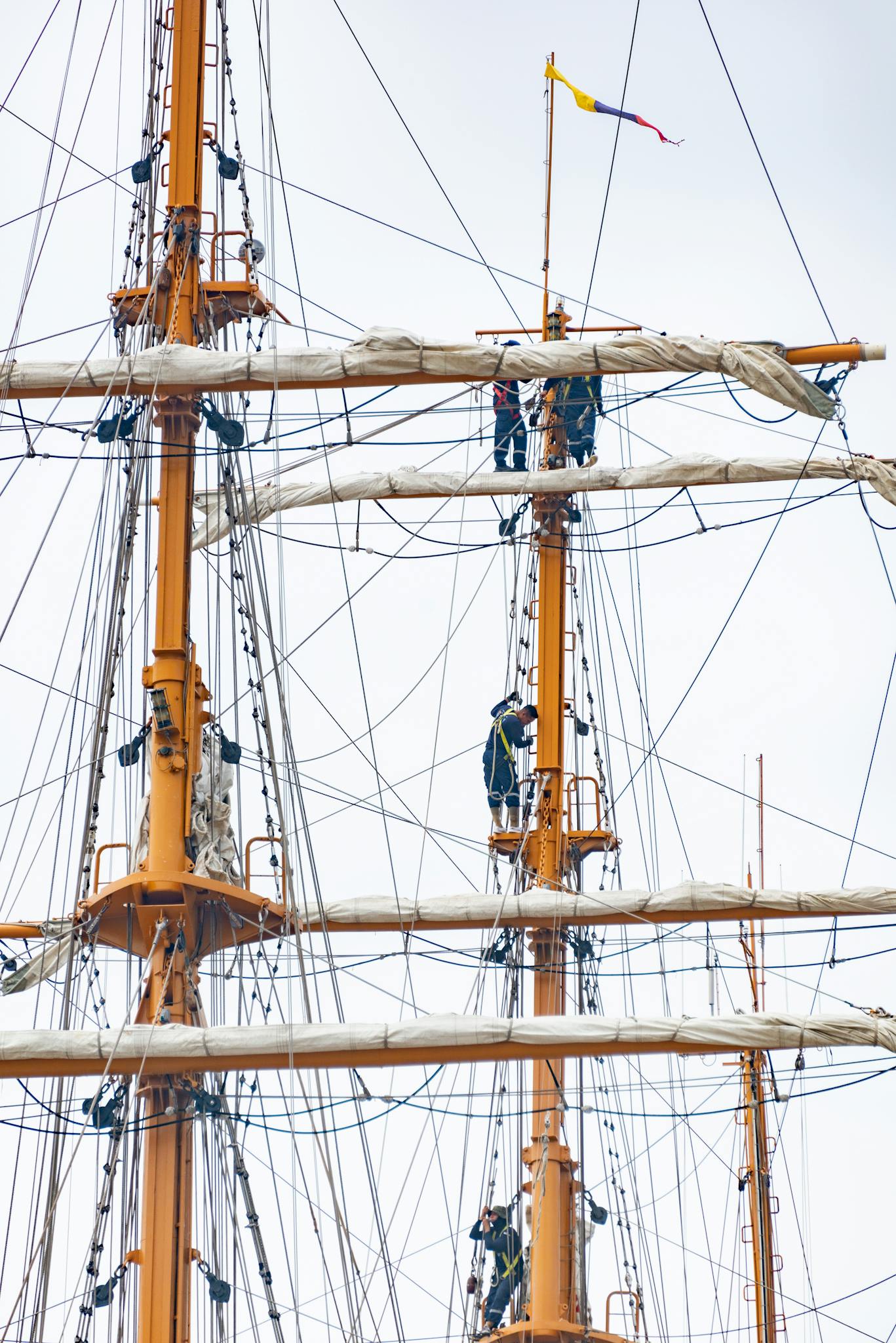 Sailors working on masts and rigging of a historic sailing ship captured in a vertical shot.