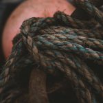 Detailed close-up of rugged, weathered ropes tied around a rusty anchor, evoking a nautical theme.