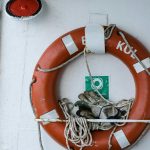 Orange lifesaver ring with gloves and rope on a ship deck, emphasizing maritime safety.
